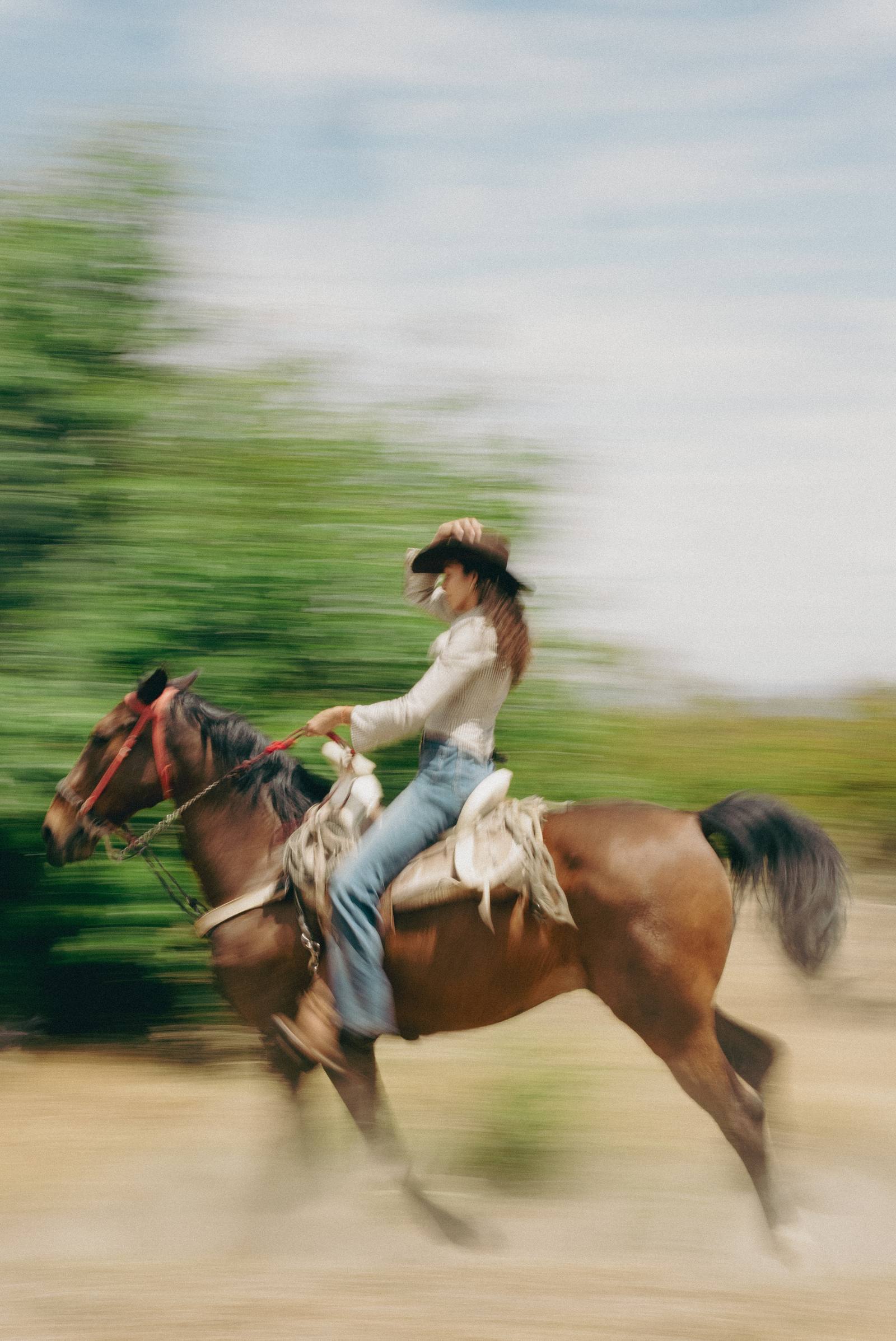 Mujer al galope sujetando el sombrero